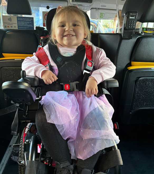 Dani-Rae smiles sat in her motorised wheelchair in the back of a taxi