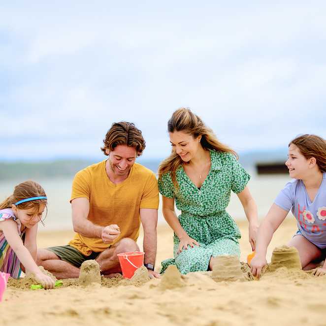 Two adults and two children are building sandcastles together on a sandy beach under a cloudy sky.
