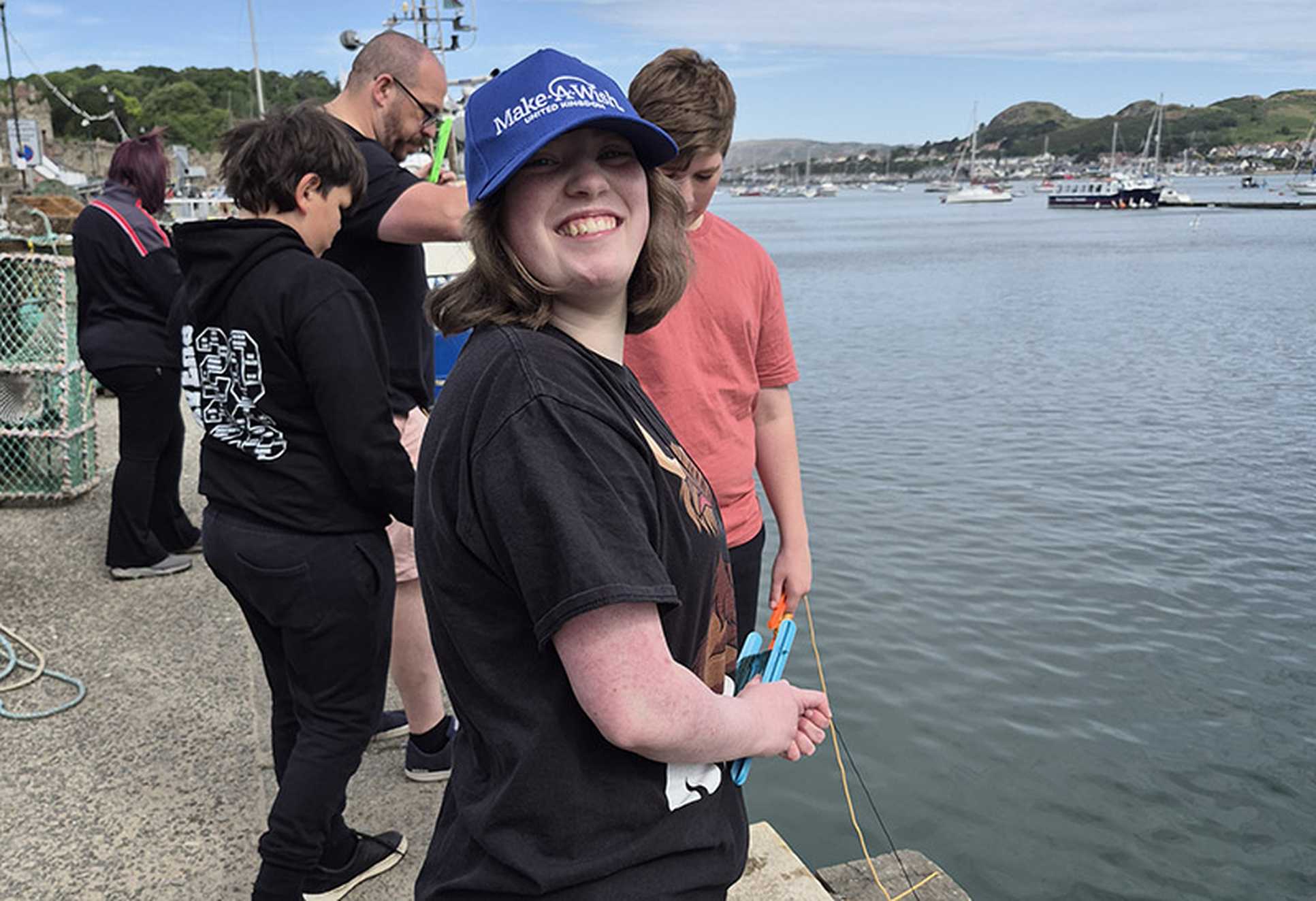 Millie smiles as she holds some crab fishing equipment alongside a harbour
