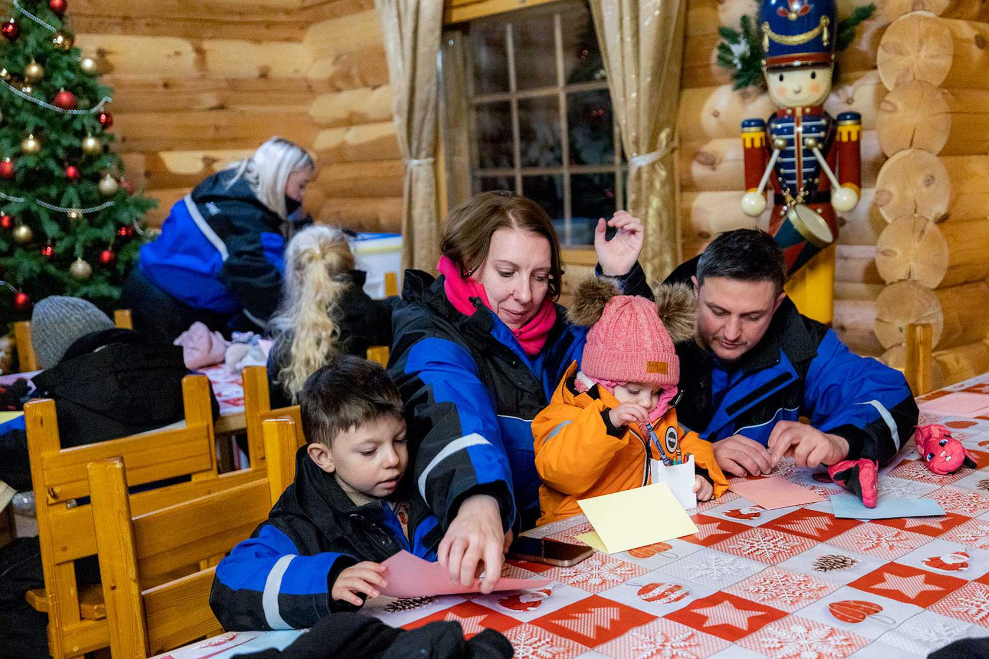 Mum and dad watching on as James and Jessie write a letter to Santa in a log cabin.