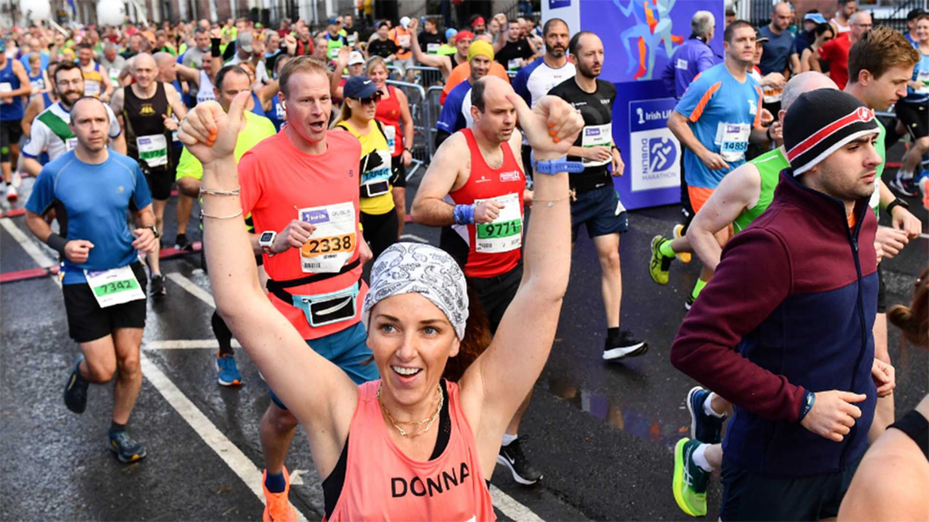 A Dublin Marathon runner smiling and waving at the camera as she passes by with other runners in the background.