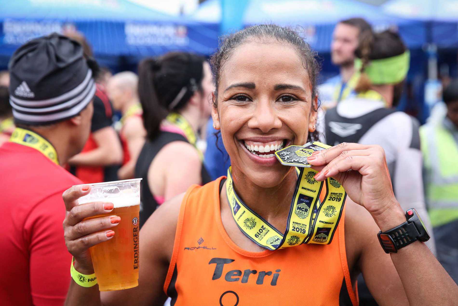A smiling Manchester Half Marathon finisher with her medal in one hand and a beer in the other.