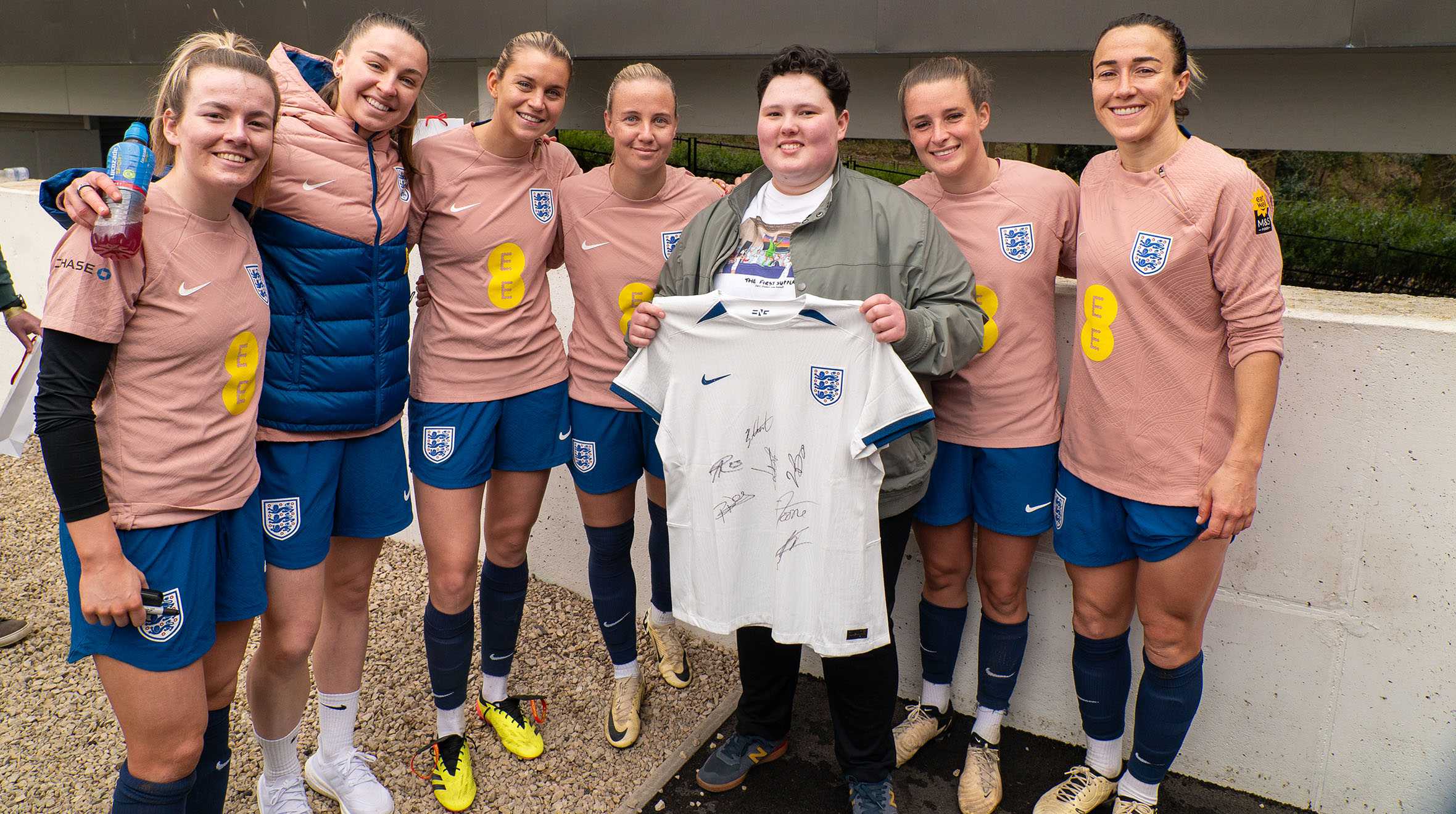 Laura holds her signed England shirt with six of the players alongside her