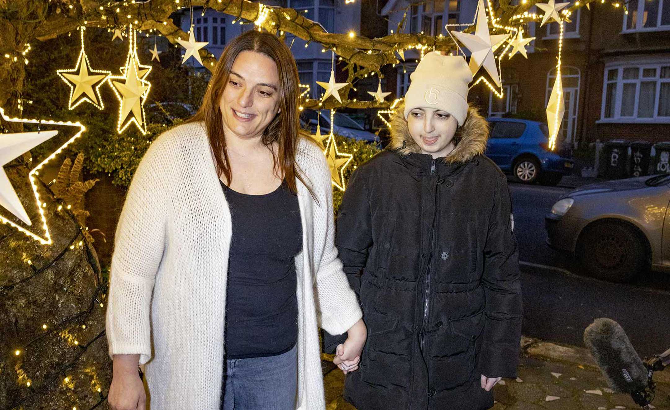 Ellie and mum, Maria standing in front of the brightly lit wish tree, outside her house.