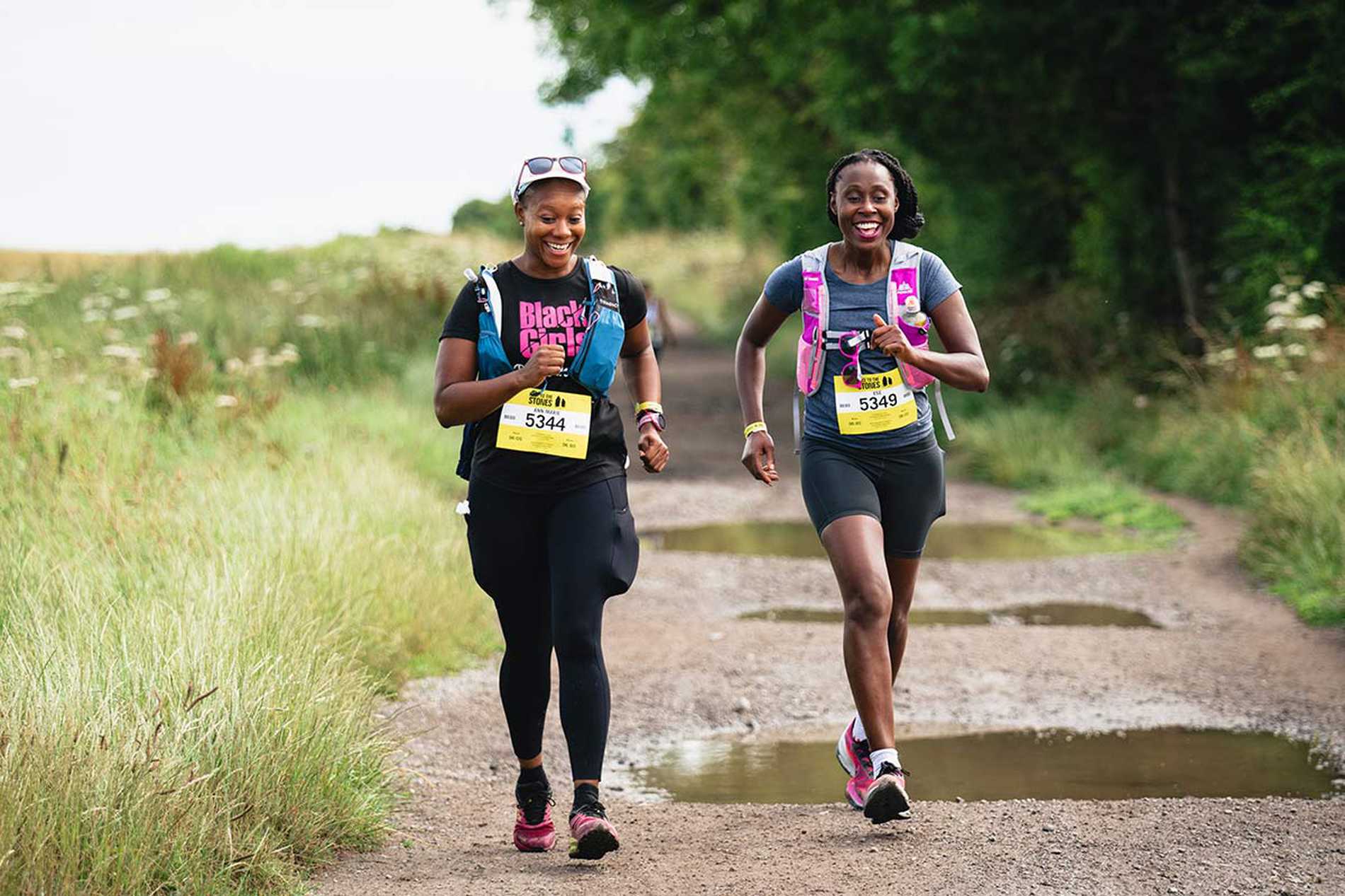 Two smiling runners making their way around puddles on a gravel track as they take on the Race to the Stones challenge.