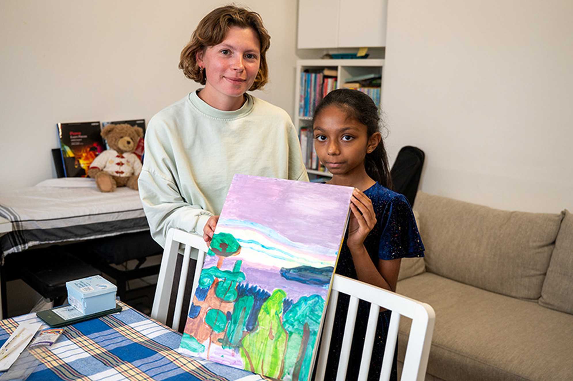Lassyhani and her art teacher are stood together facing the camera. Between them, they're proudly holding Lassyhani's latest oil painting. A vibrant display of purple and various shades of green.