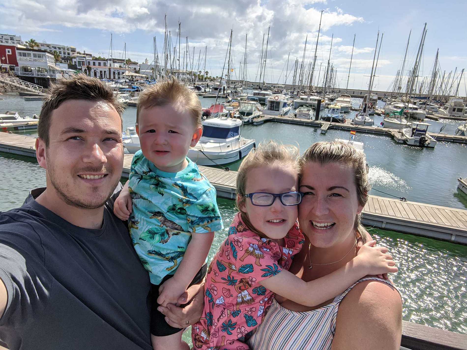 Hope with her mum, dad and brother standing by the harbour, with boats in the background.