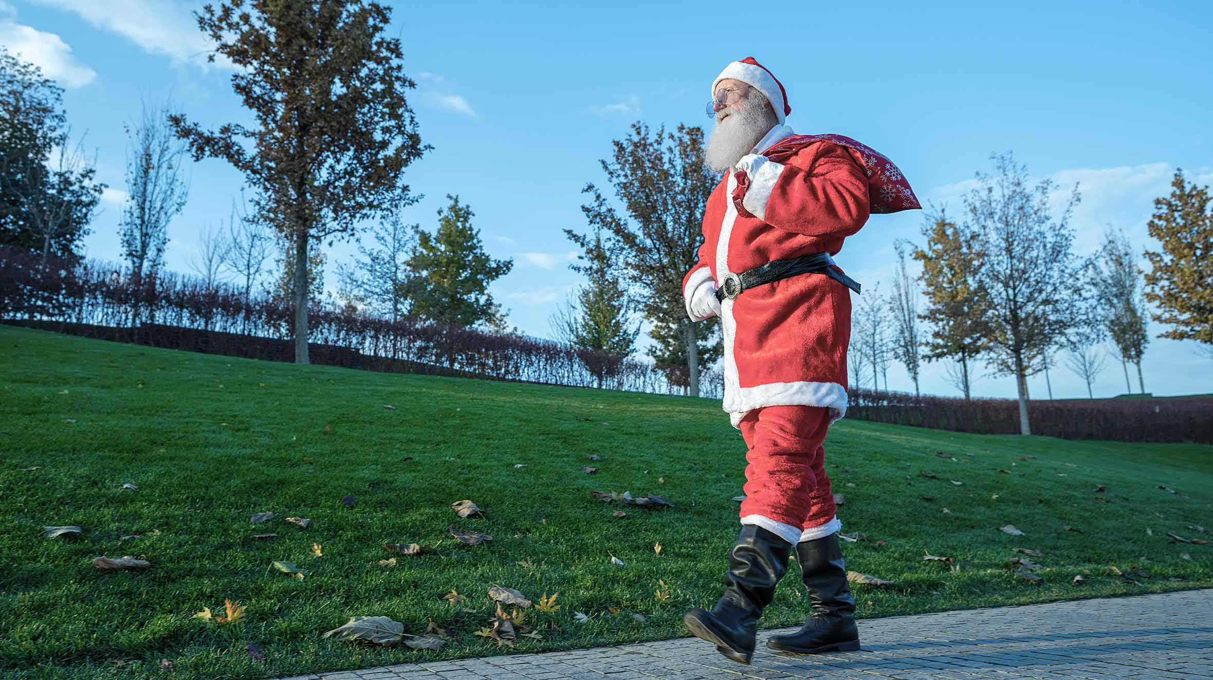 A man dressed as Sant, walking through a park.