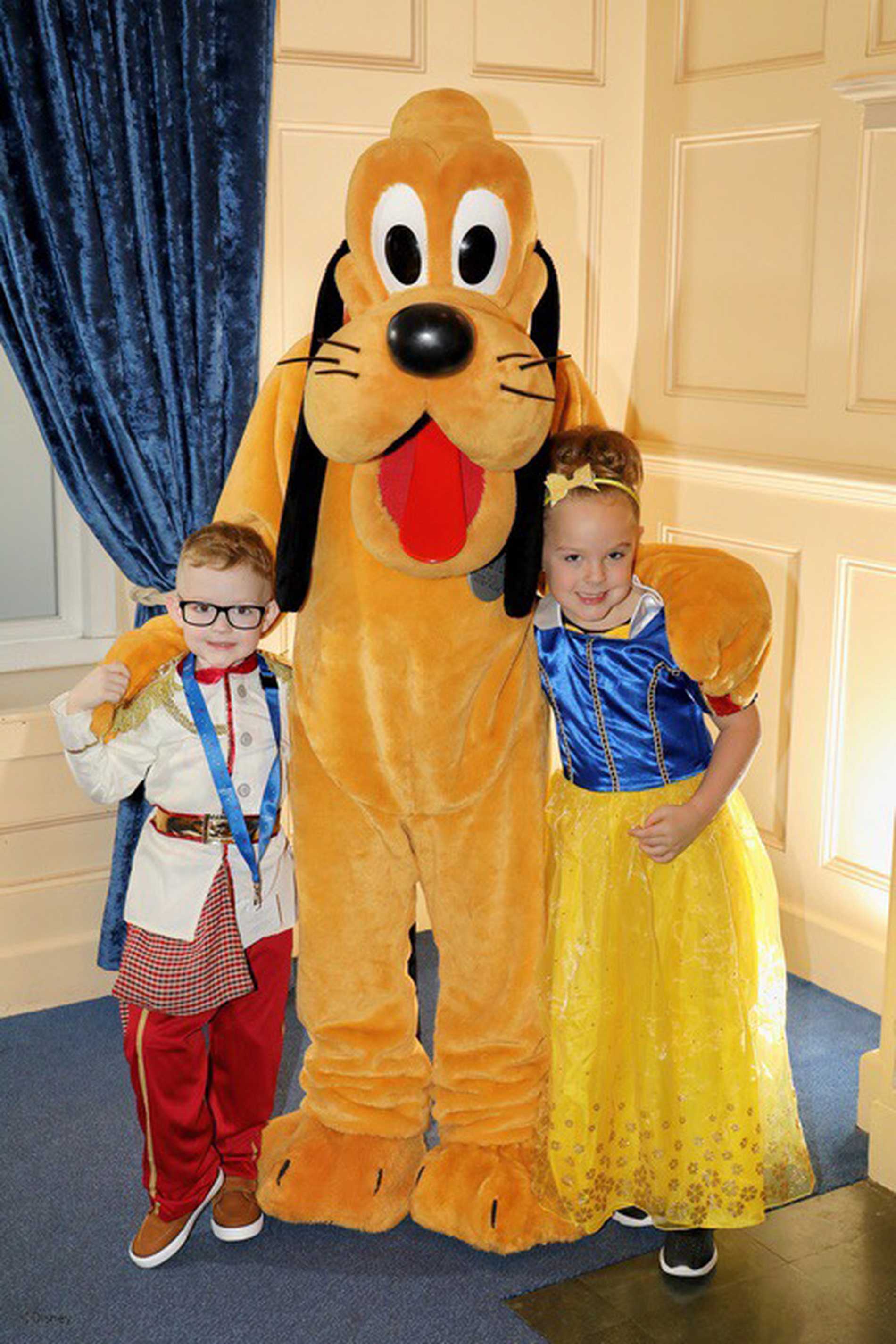 Patrick and his sister dressed in costumes, posing with Goofy.