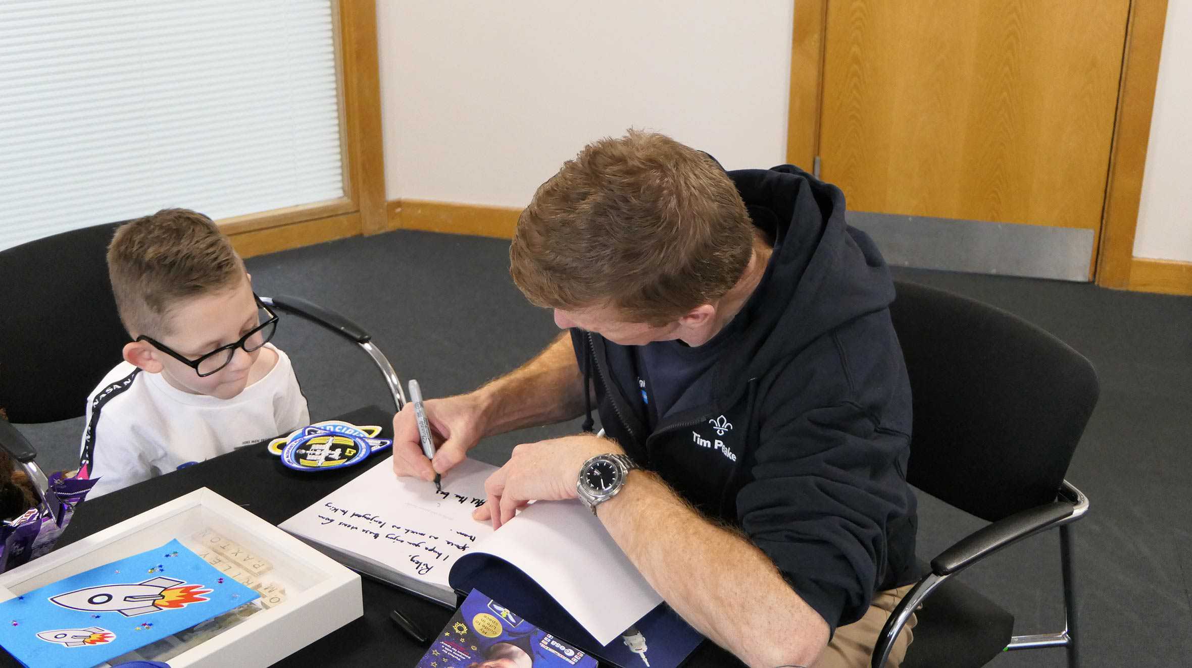 Astronaut, Tim Peake signing a book for wish child, Riley.