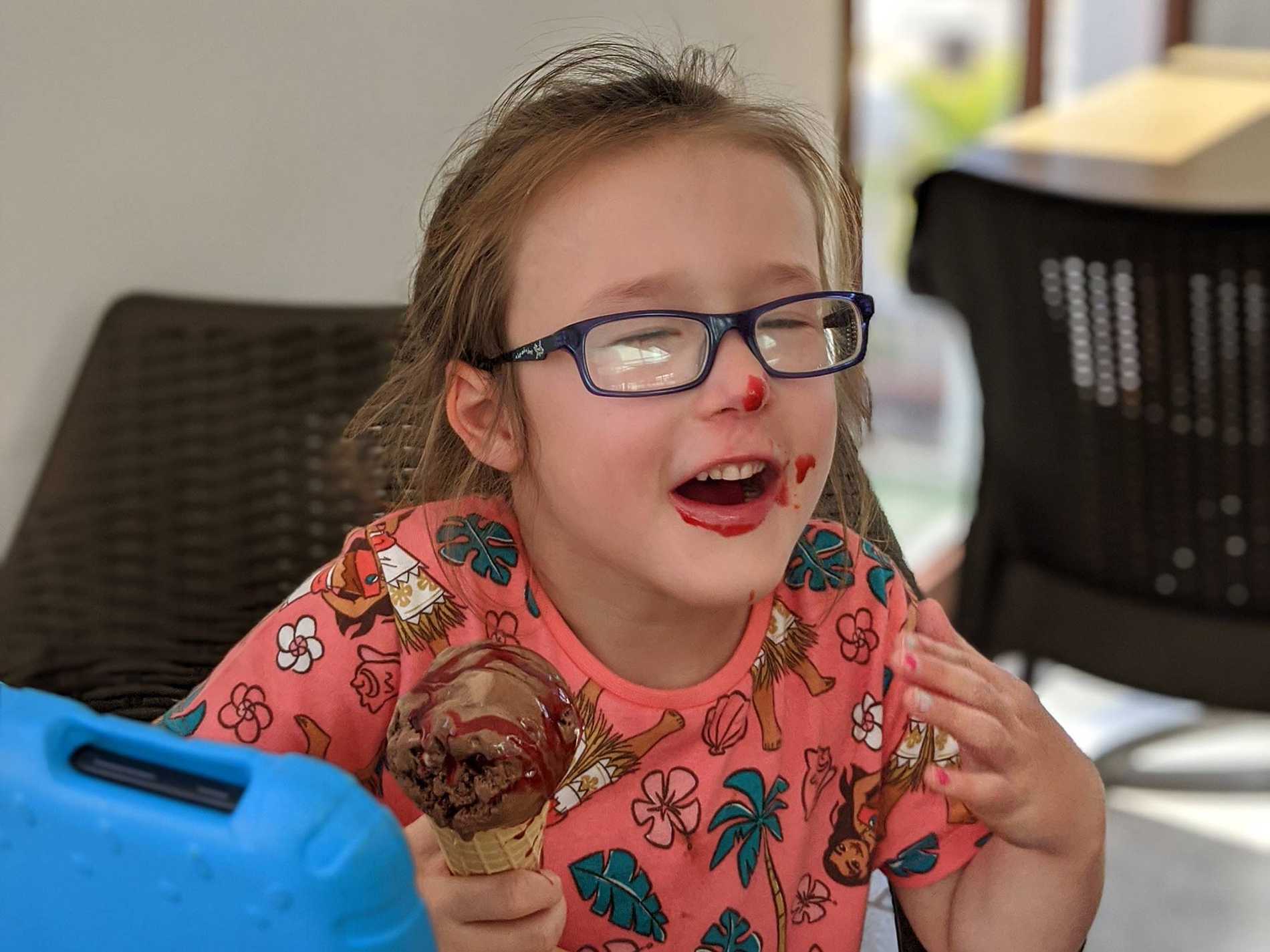 A smiling Hope, eating a cornet with ice cream around her mouth.