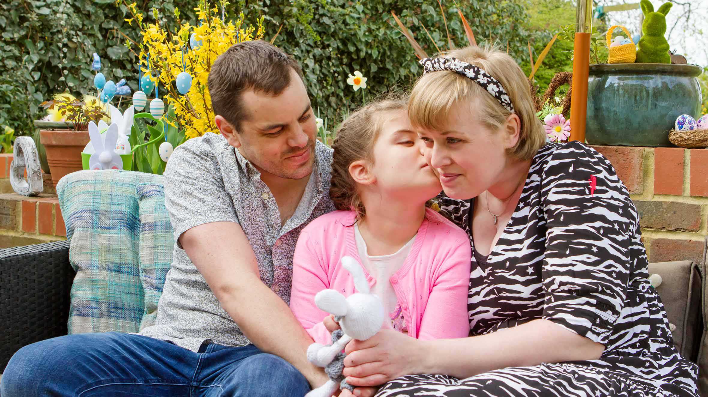 Gracie, sitting on a bench with her mum and dad and kissing her mum on the cheek