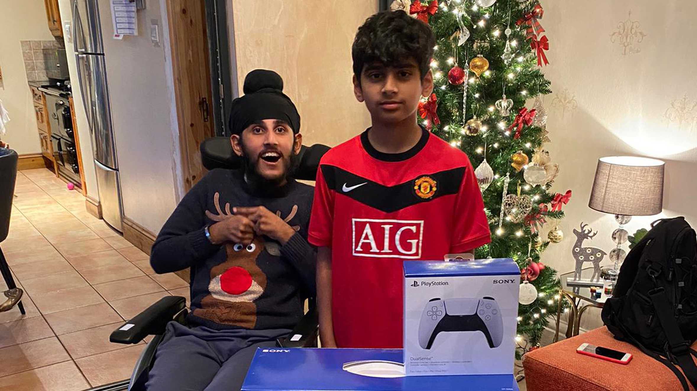 Sunil and his brother, Rav, posing in front of the Christmas tree with his PS5.