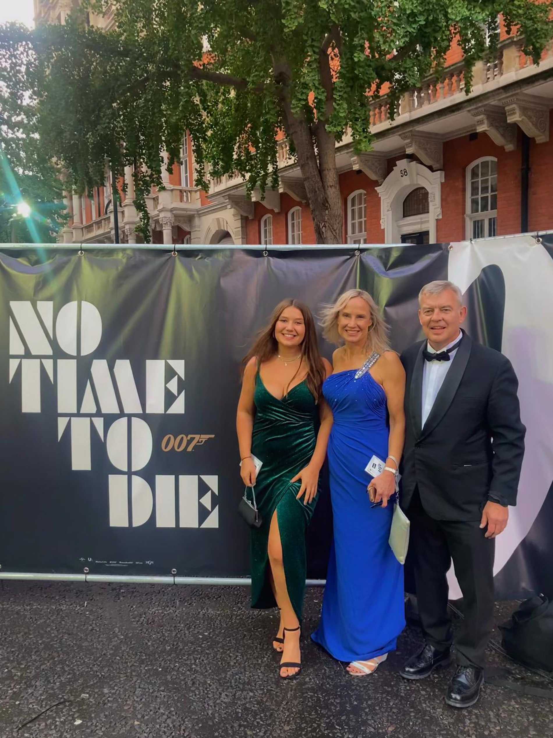 Chloe and her parents posing next to a 'No time to die' banner.