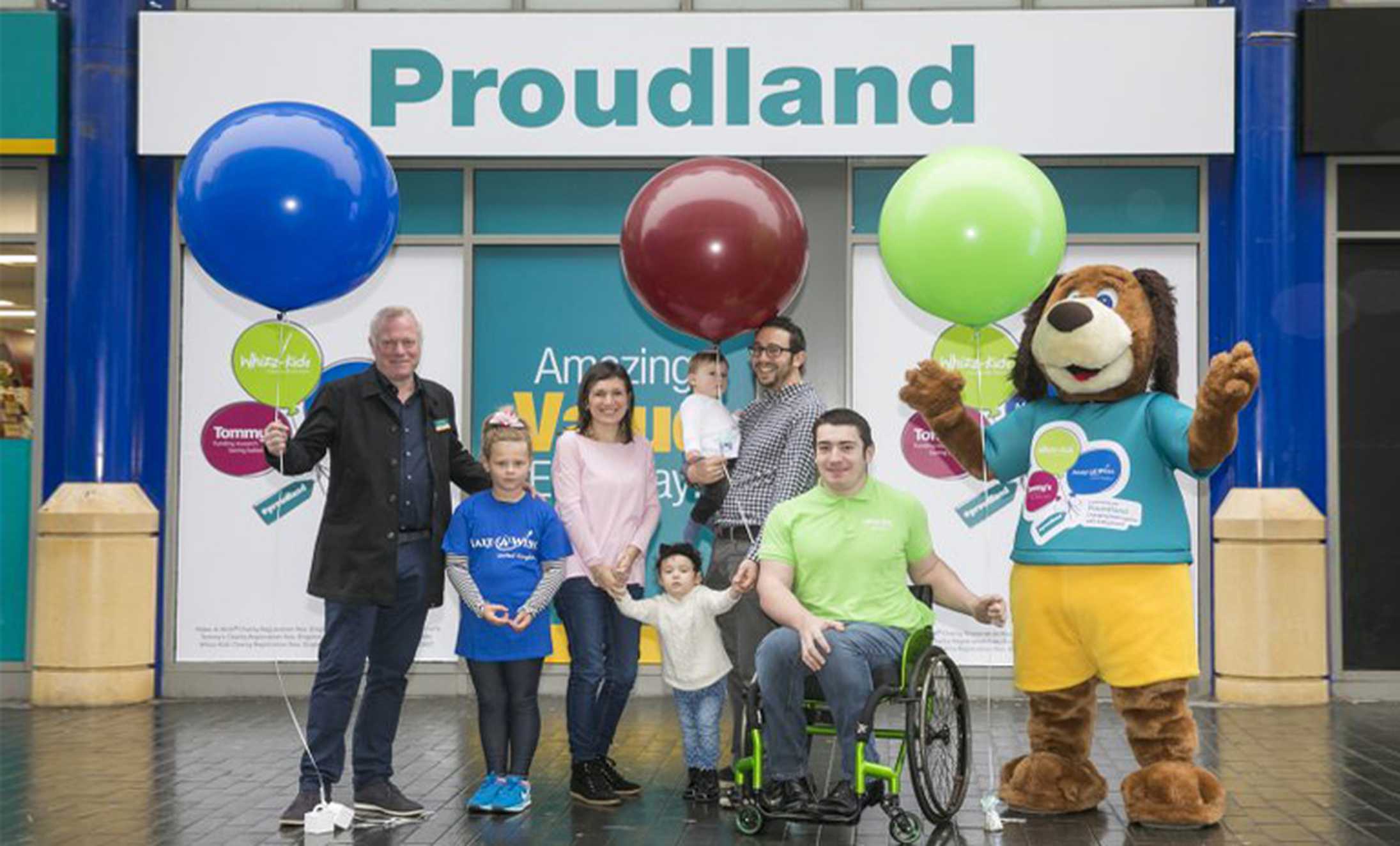 A group of smiling Proudland fundraisers holding colourful balloons.