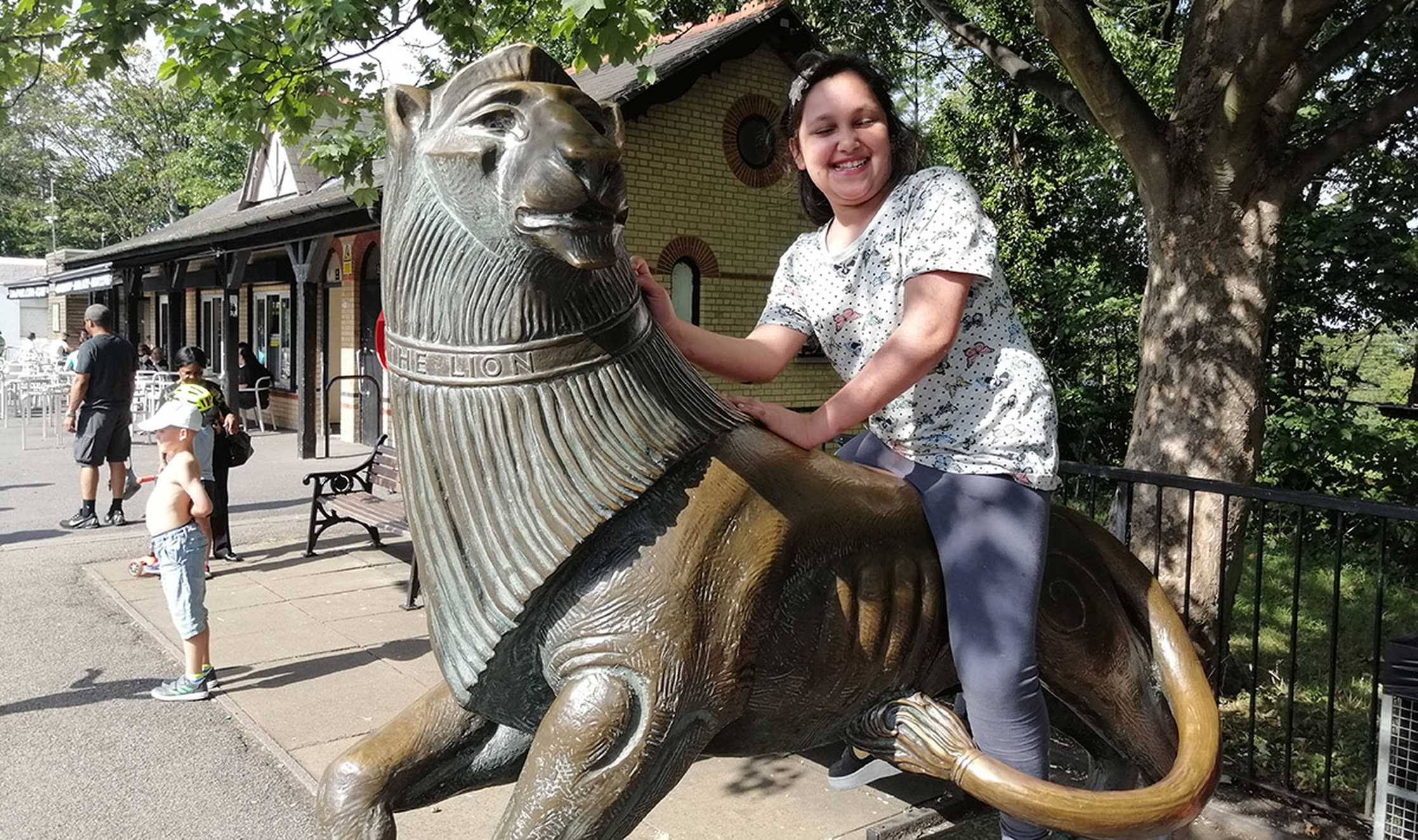 Before her illness, Sumaiya sits smiling sat on a large brass lion