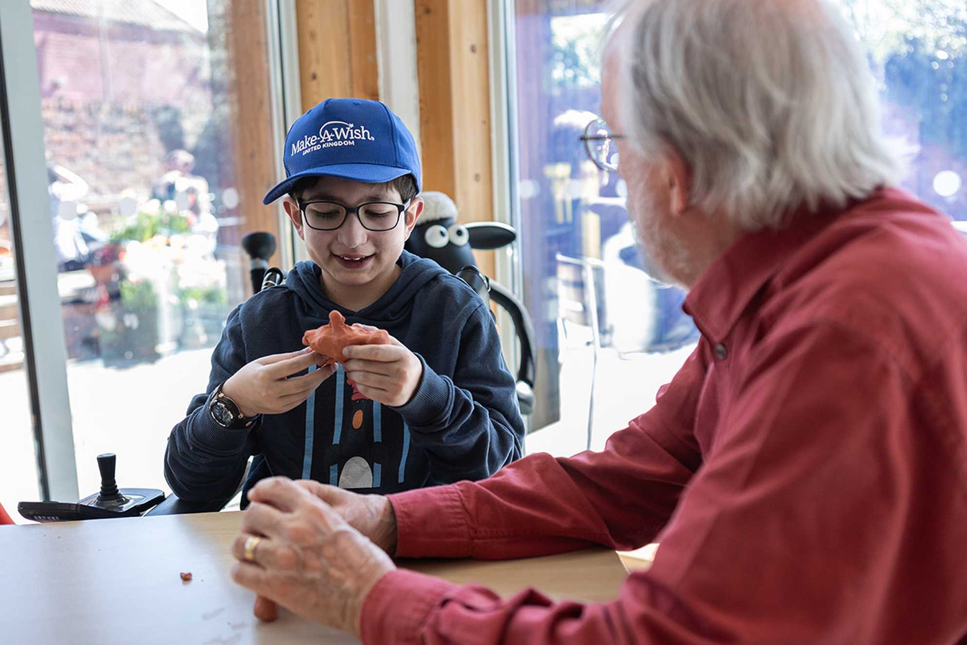 Mert smiles while creating a clay Morph figure sat next to Peter Lord from Aardman