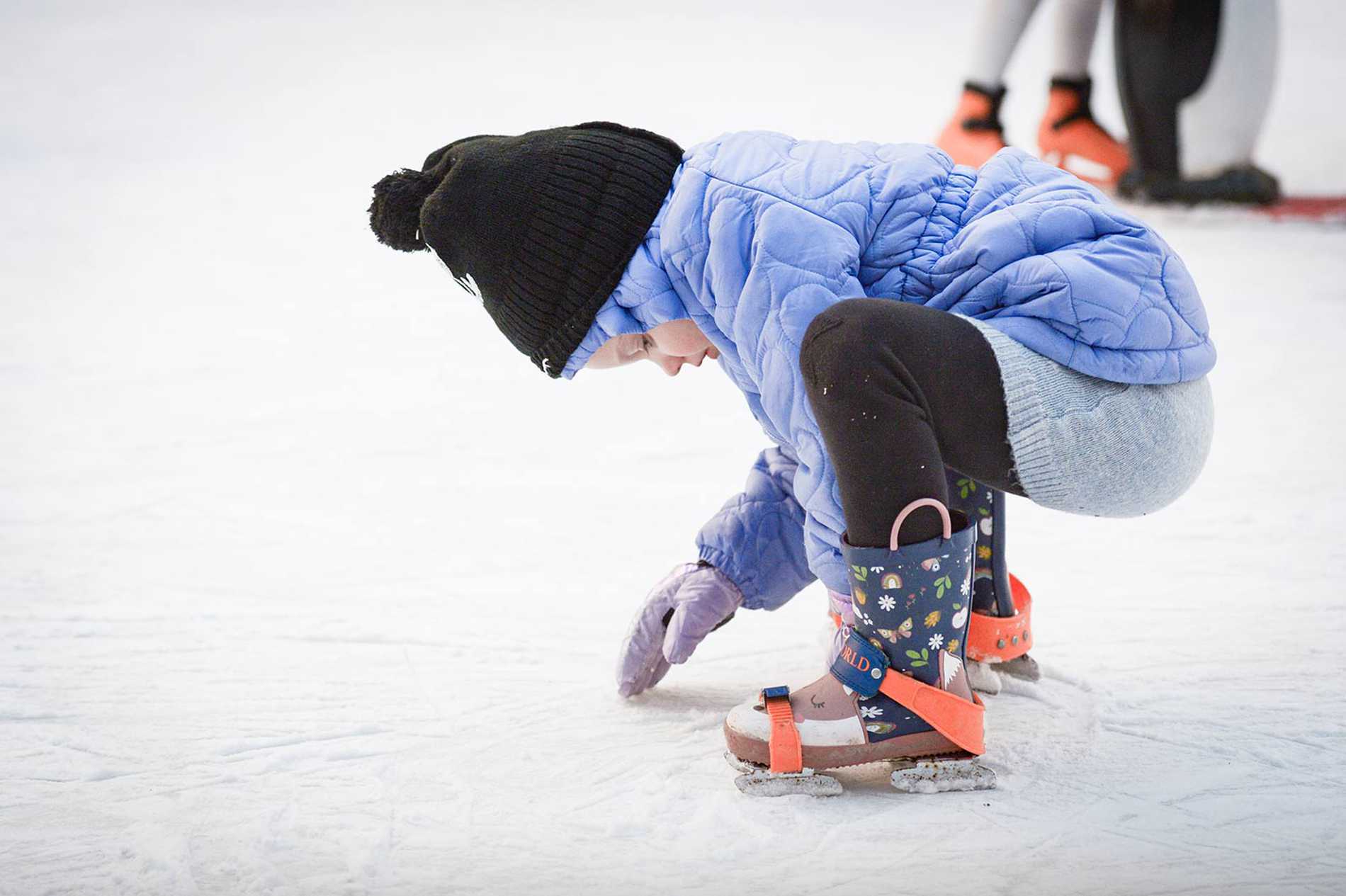 Julia bending down to touch the ice while on the ice rink.