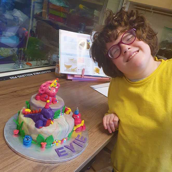 A smiling Dakota, proudly showing off a dinosaur-themed cake she's made.