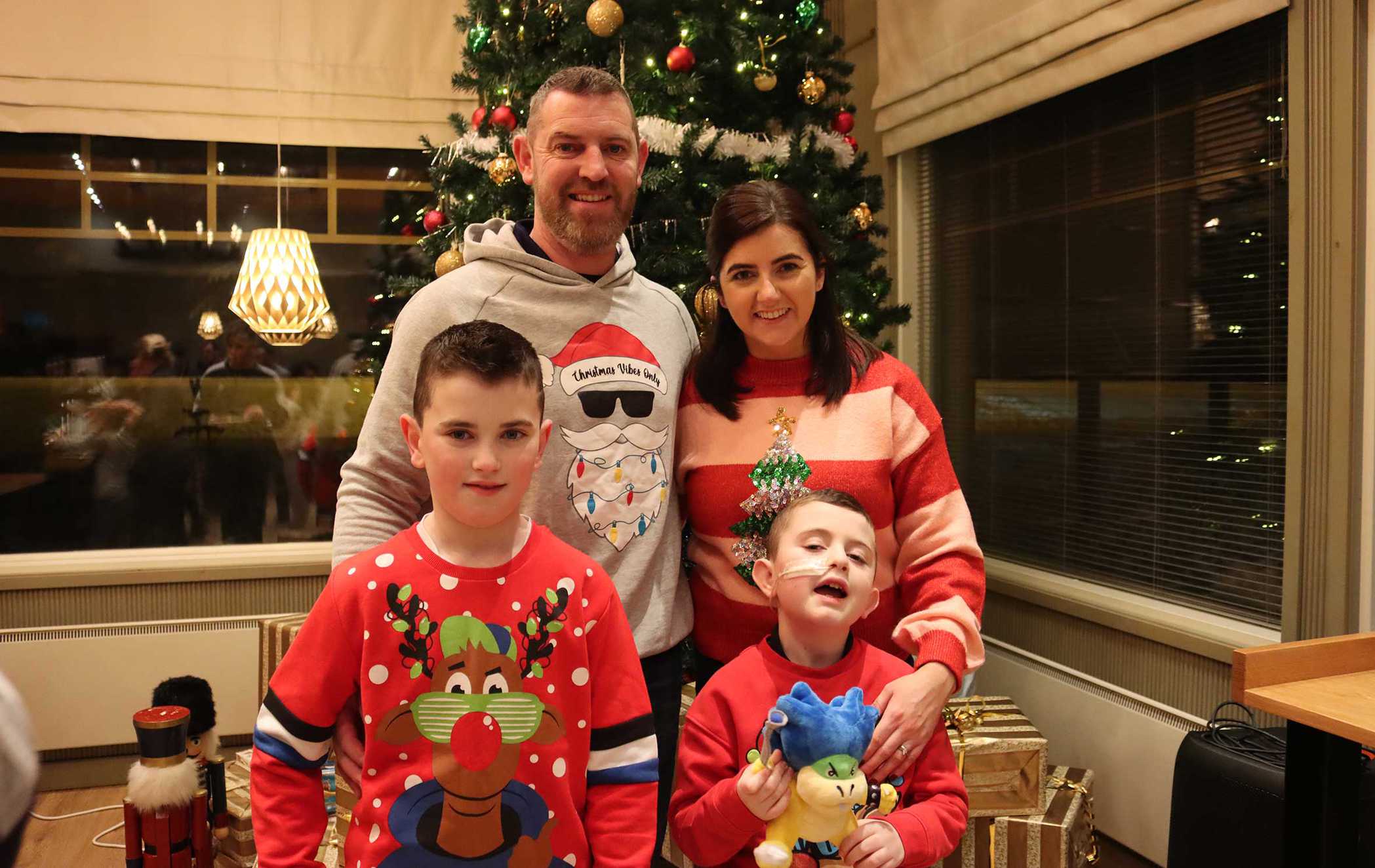 Tíernan standing in front of a Christmas tree with his mum, dad and brother, all earing Christmas jumpers.