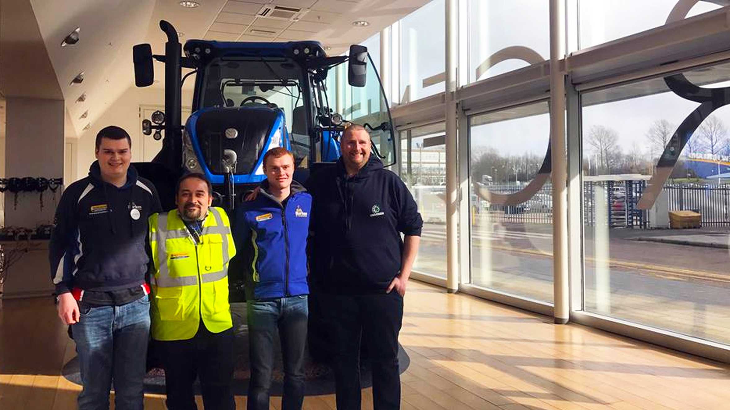 James smiling with employees smiling in front of a big tractor