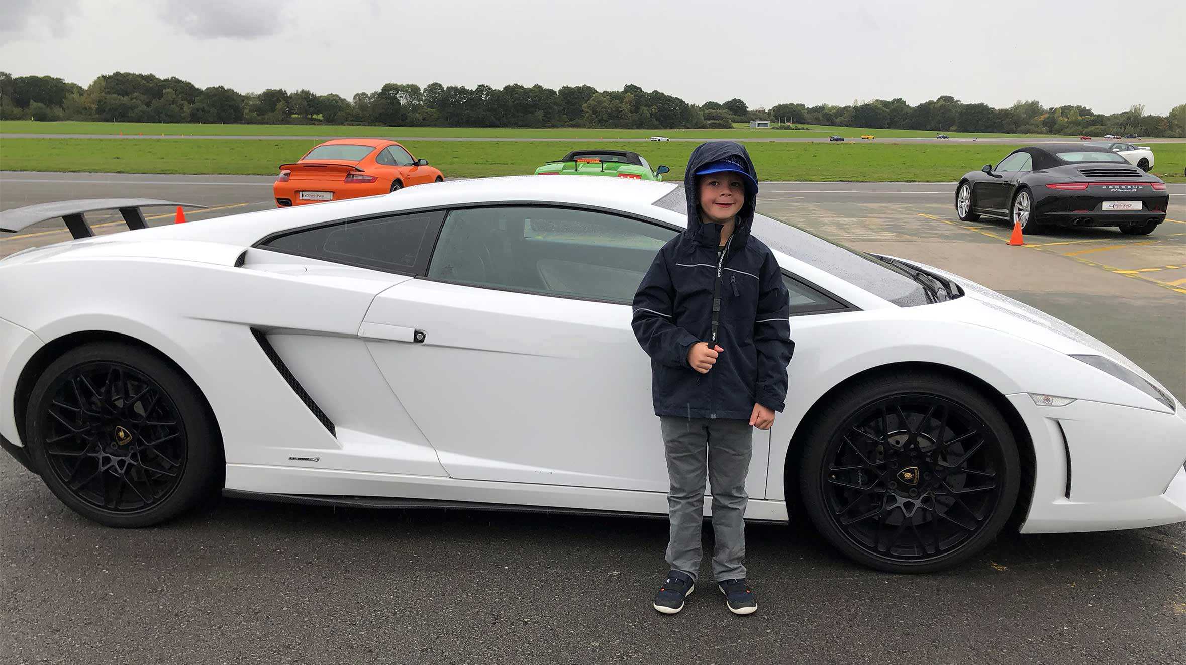 Alex standing in front of a white Lamborghini, with other sports cars in the background