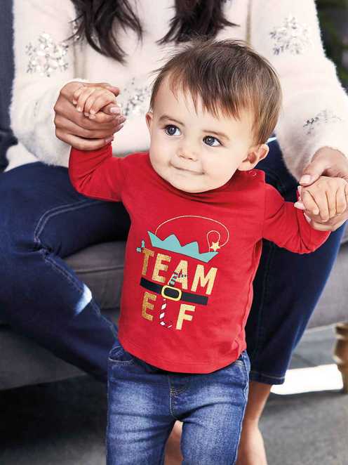 Young child wearing a red 'Team Elf' long-sleeved t-shirt.