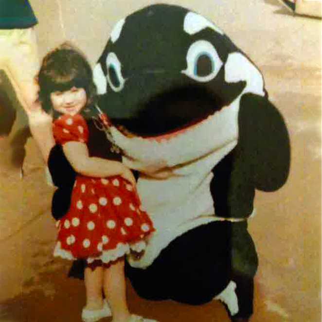 Charlotte, wearing a red spotty dress, posing with an Orca character.