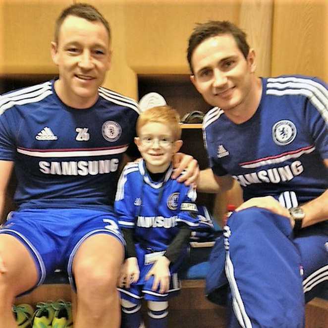 Oscar, wearing his Chelsea kit, sitting between John Terry and Frank Lampard in the Chelsea changing room.