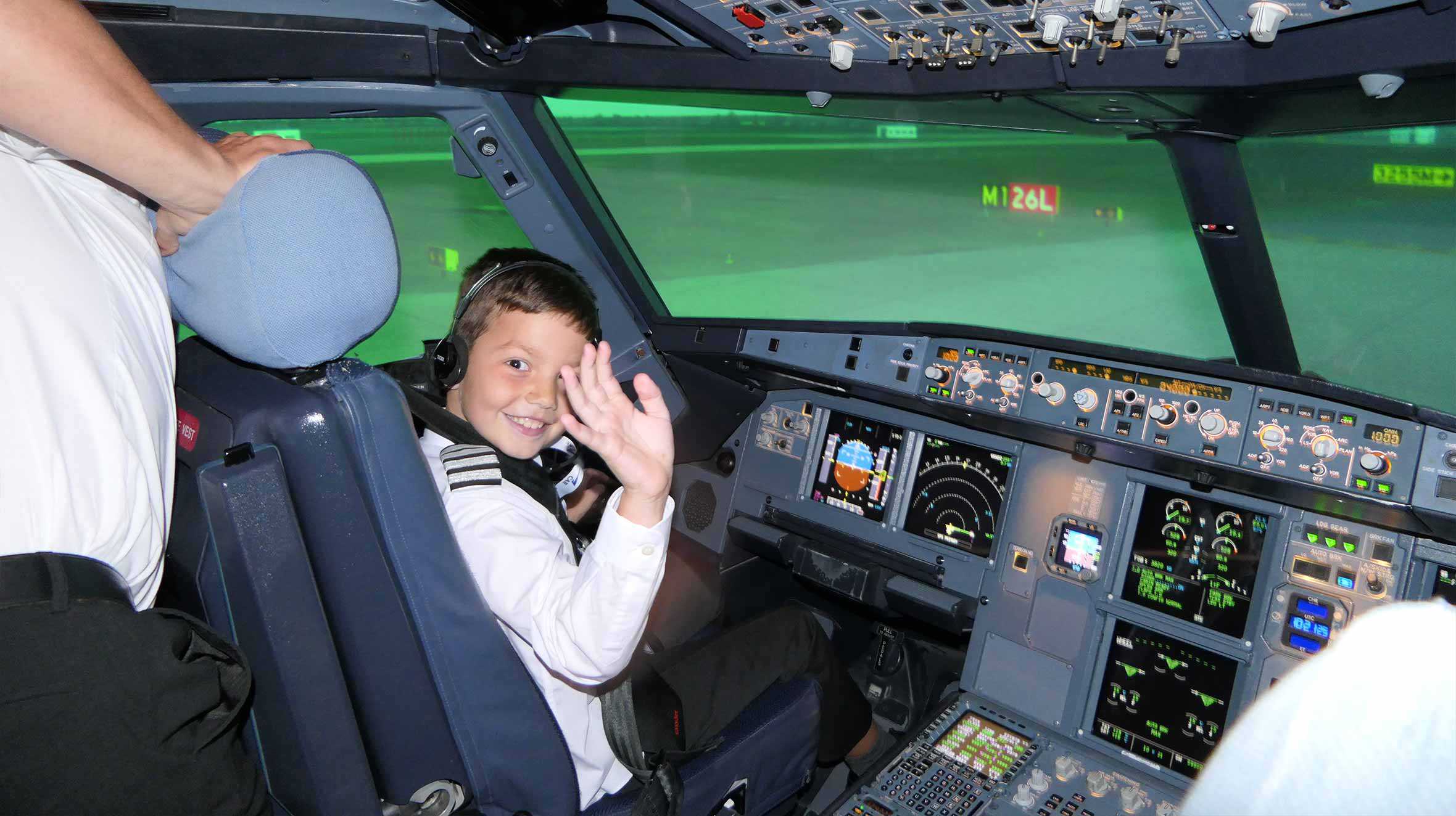 Jacob waving and smiling sat in a pilot simulator