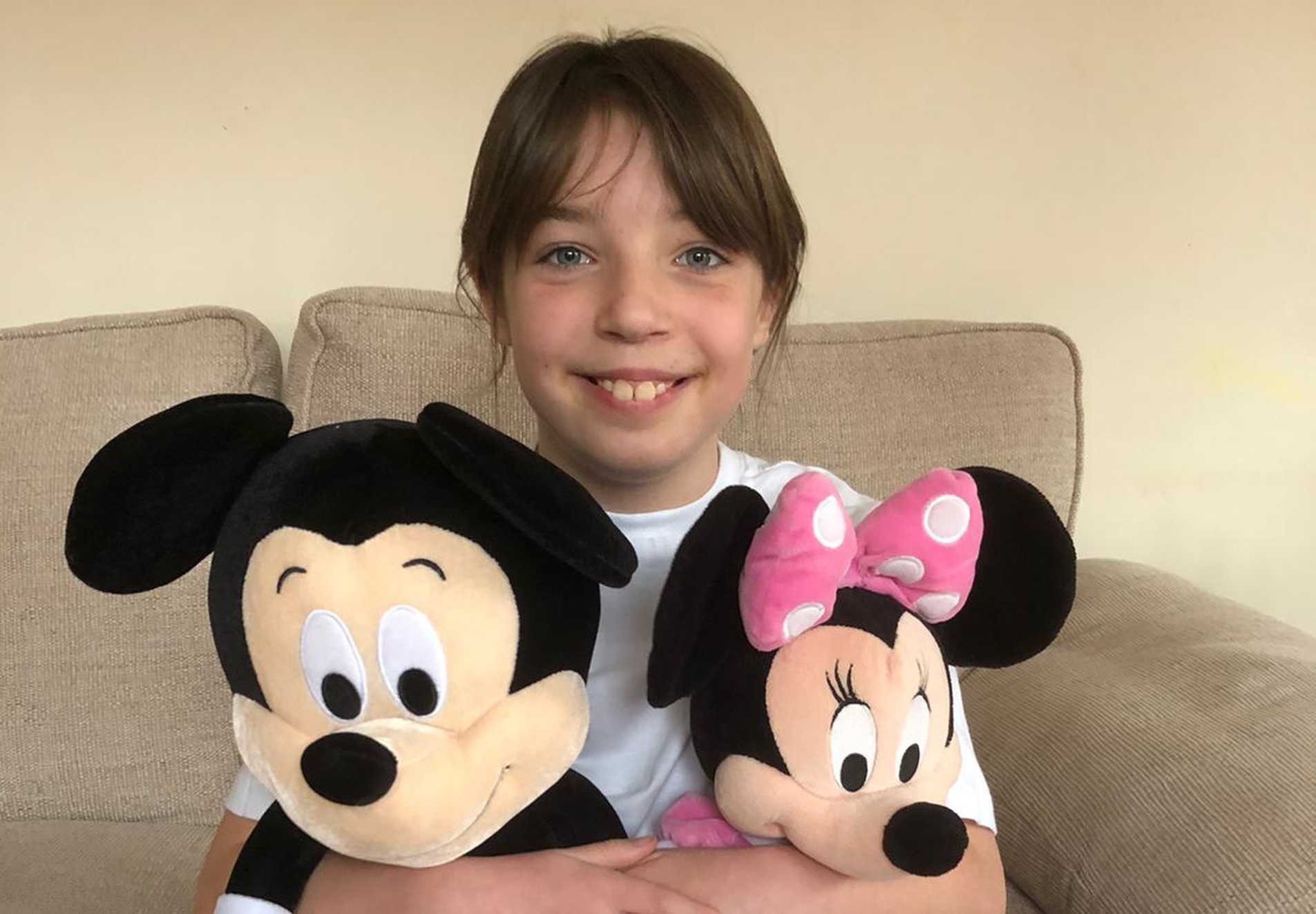 Emily sitting on her sofa, holding a pair of Mikey and Minnie Mouse dolls.