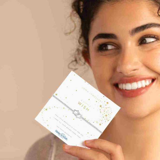A woman smiles while holding a card with a star bracelet and the words "A Little Wish" printed on it.