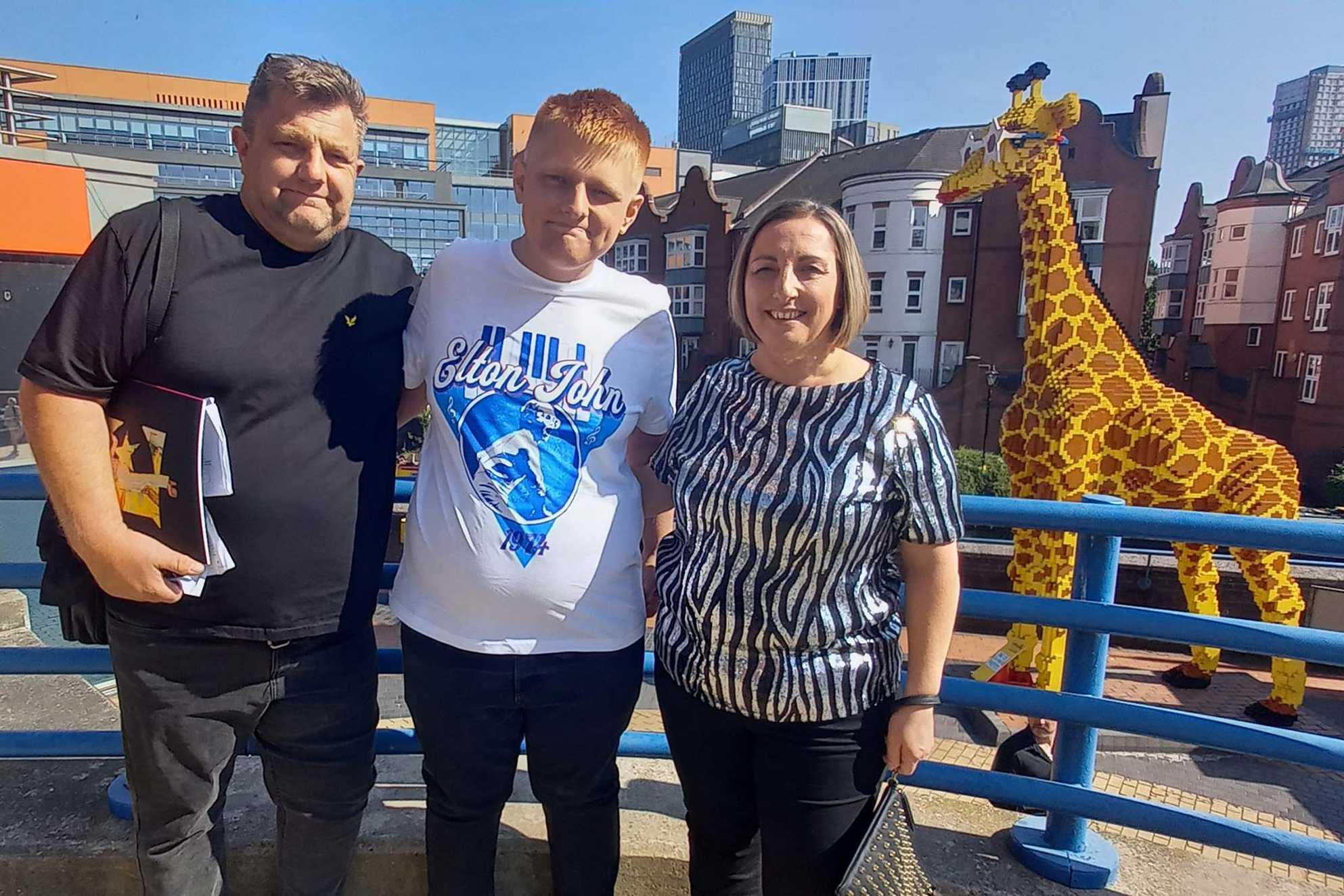 Oliver and his parents posing next to a large giraffe made from LEGO.