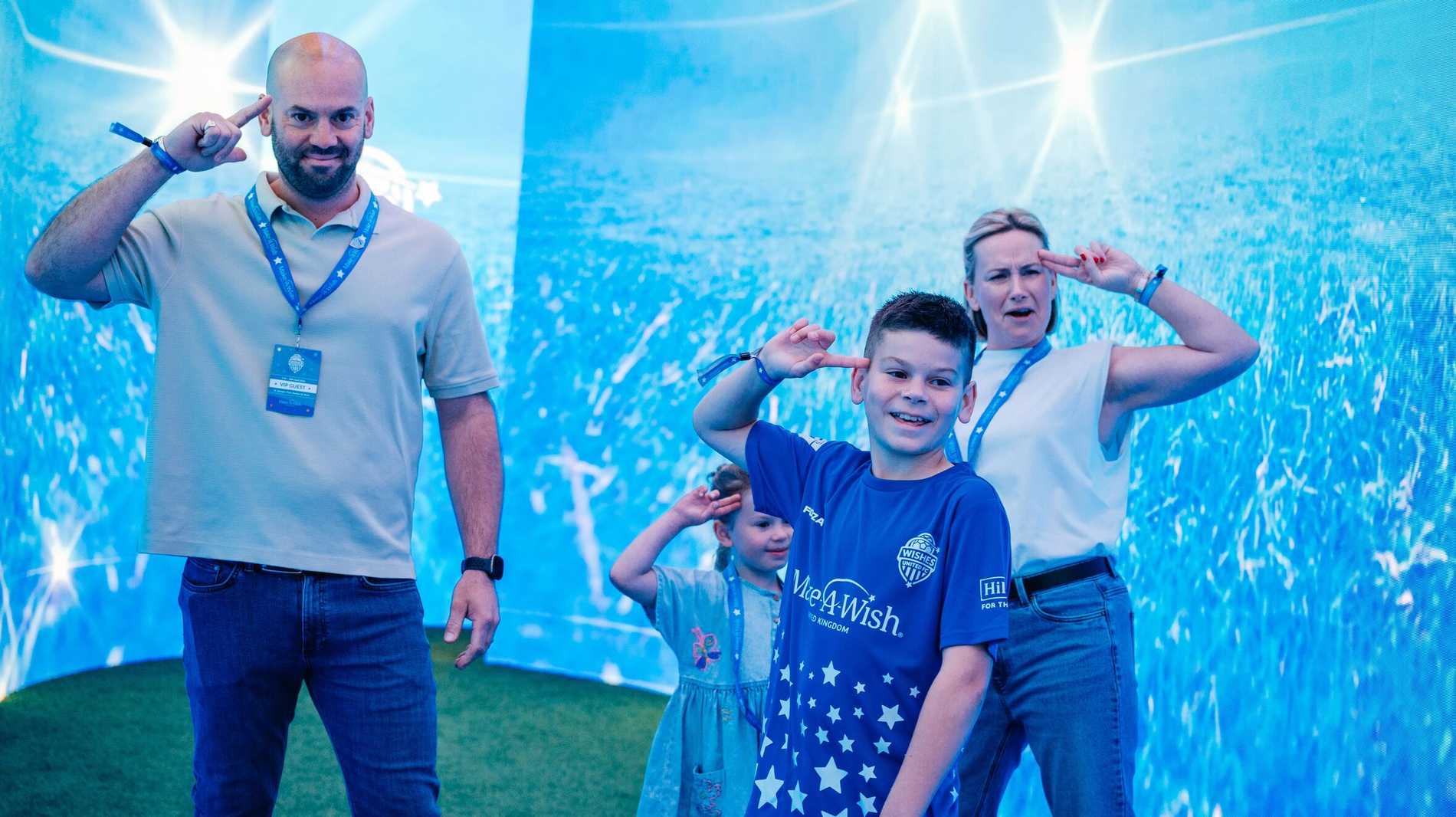 Finlay celebrates with his family by pulling his pose.  Pointing his finger to his temple.  To his sister and his dad are also pulling the pose and to his right his mother is too.