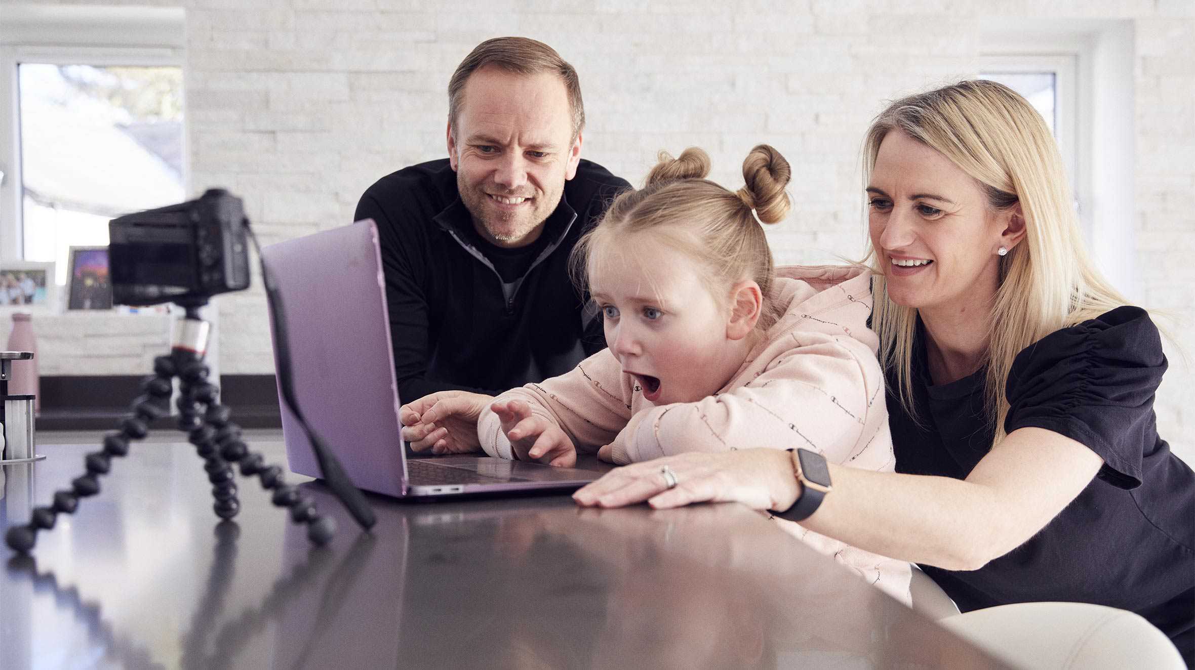 An excited Isla sitting with her parents while she plays on her new laptop.