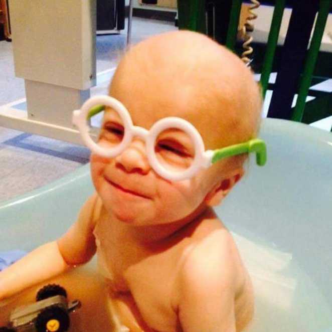 Jack enjoying a bath as a baby, wearing a large pair of green and white round-framed glasses.