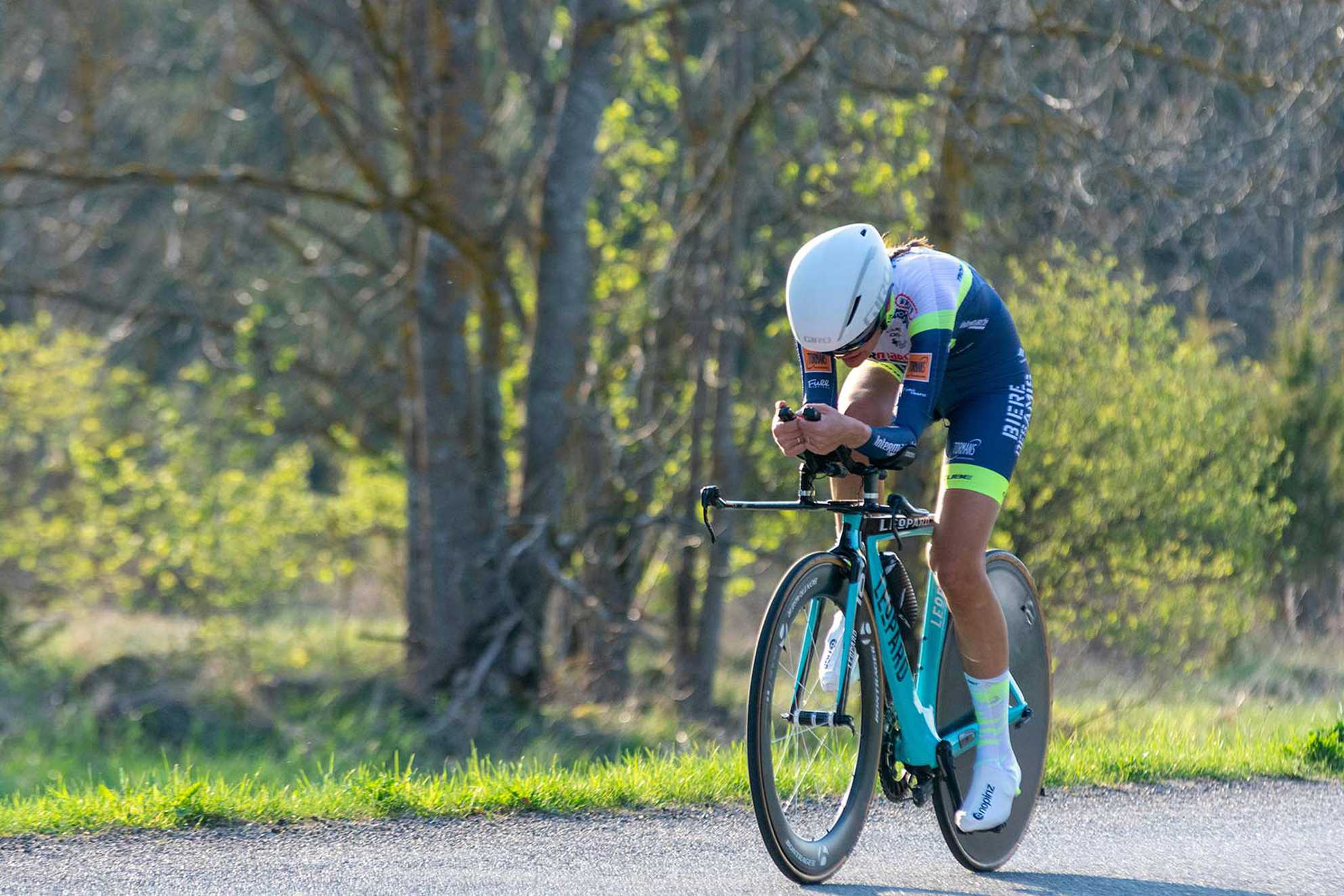 a competitive female cyclist tucked into her aero bars as she cycles along a country road.