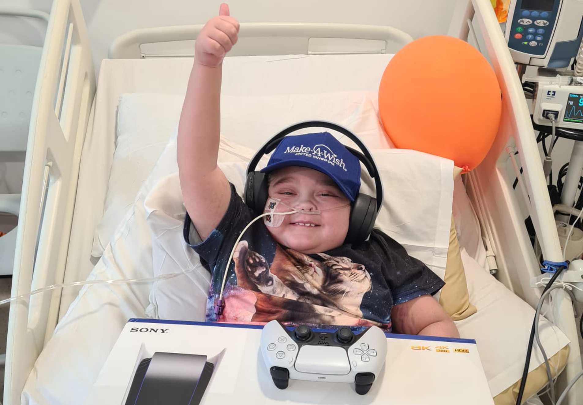 Zakk giving a big thumbs up from his hospital bed while holding his new PS5.