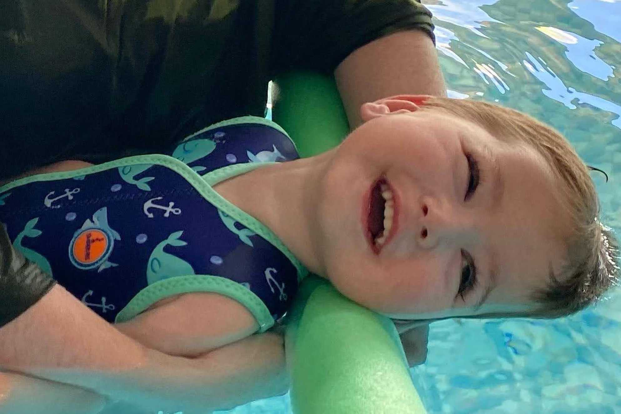 Oliver smiling as he floats in his spa pool with his mum's arms supporting him.