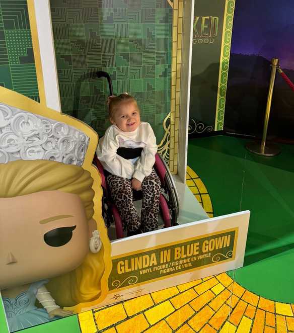 Dani-Rae smiles while sat in a novelty, oversized Wicked-themed Funko pop box