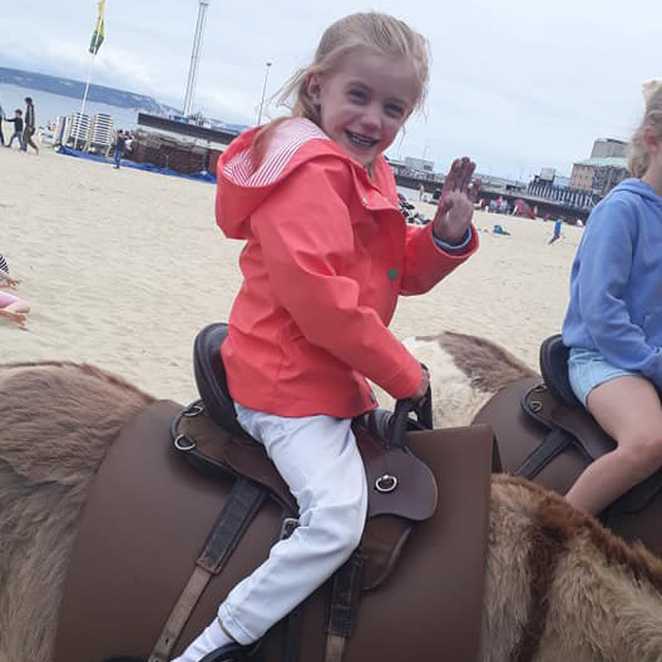 A smiling Ava enjoying a donkey ride on the beach.