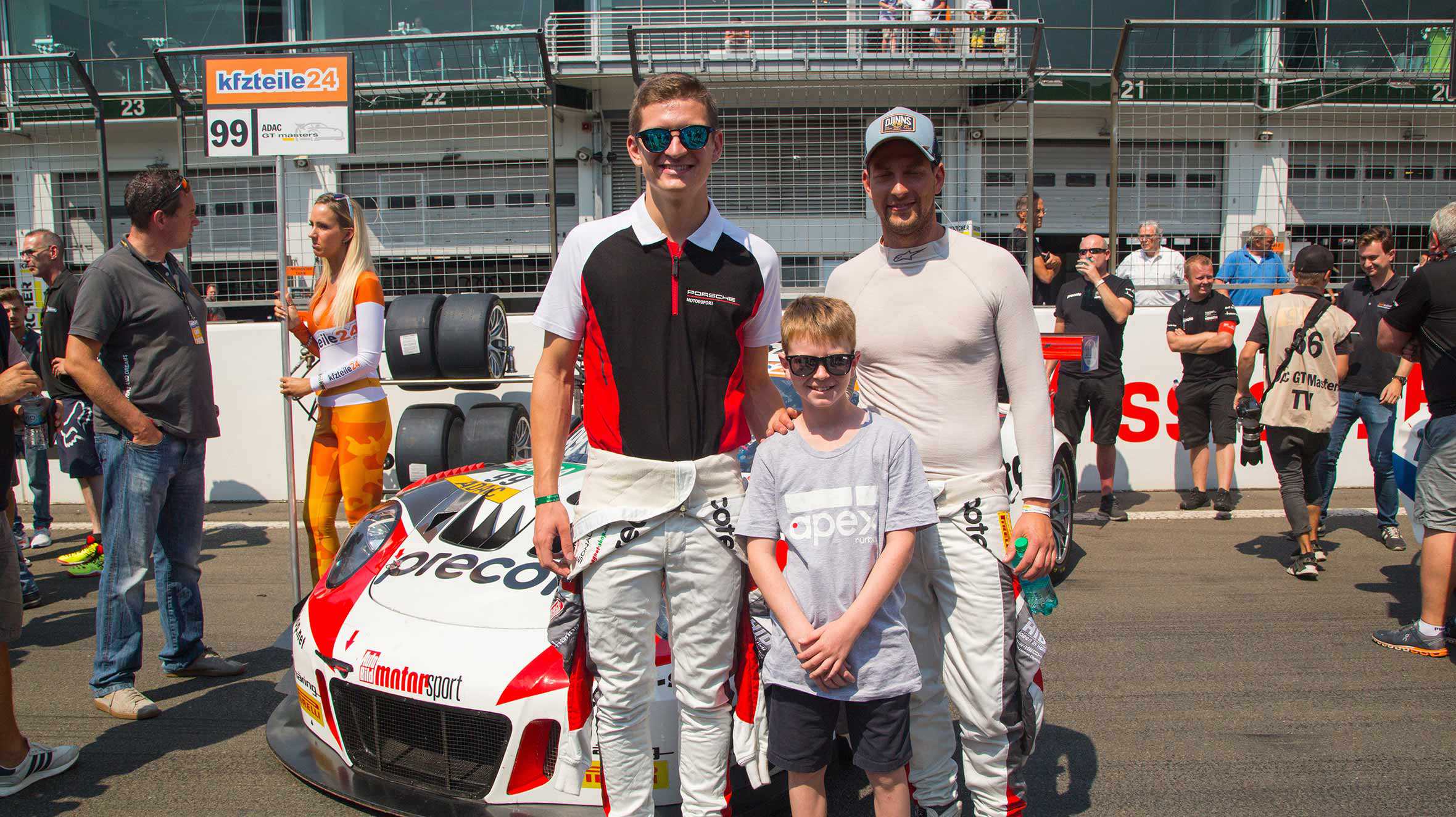 Dewi posing in front of a racing car with two drivers