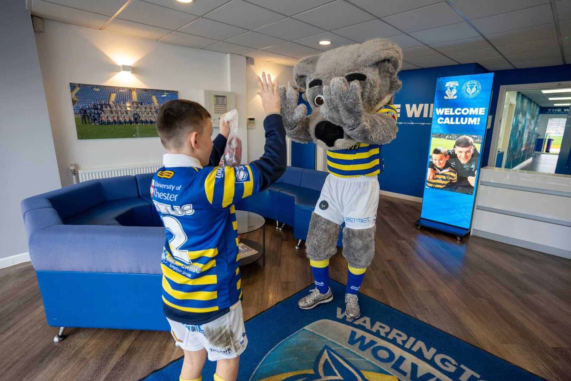 Callum gives Wolfie the mascot a double high five in the reception area of the stadium