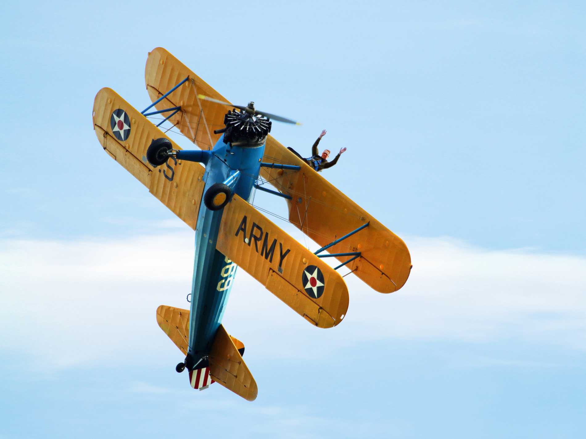 A bi-plane climbing vertically with a brave wing walker firmly attached.
