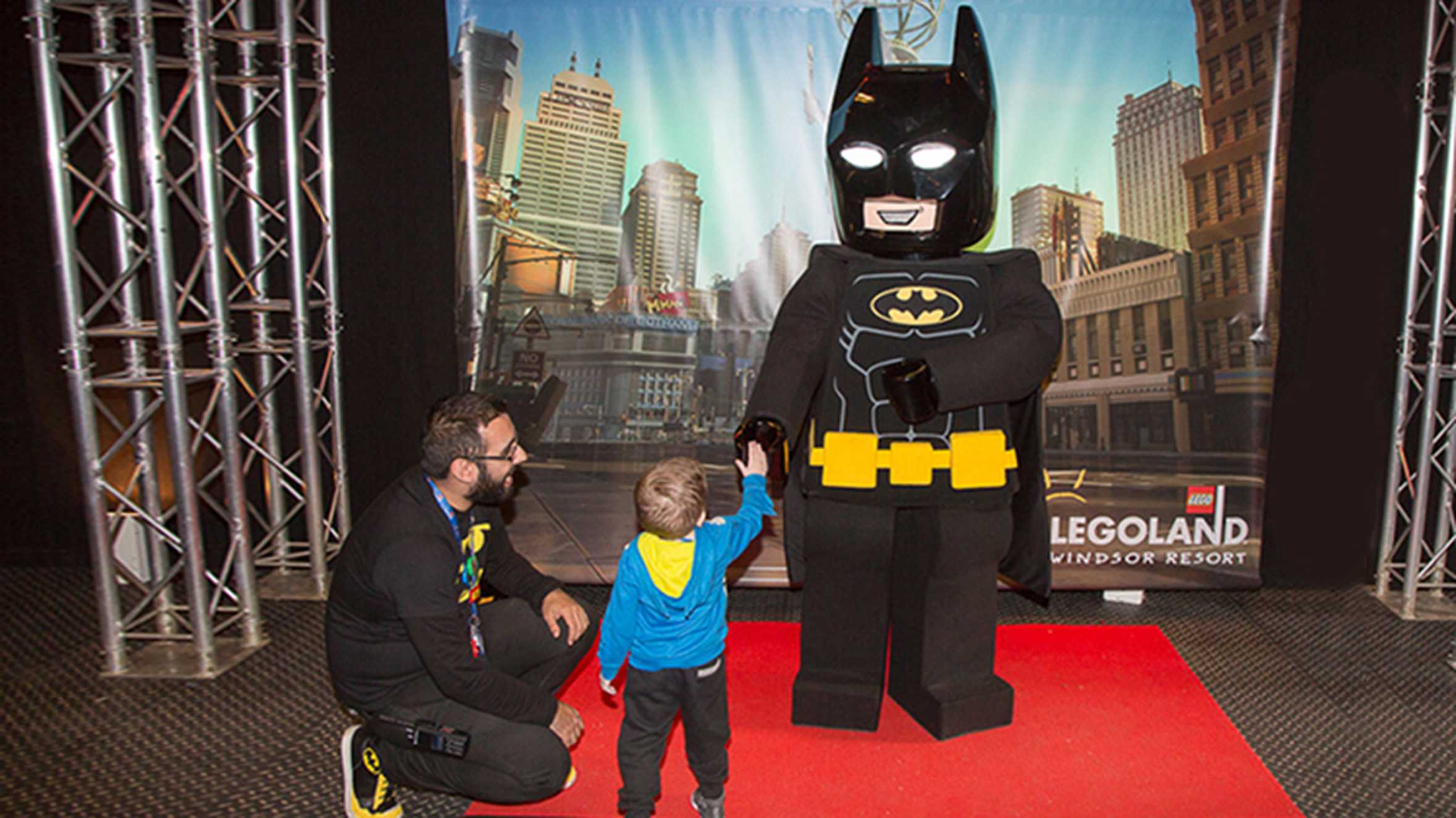 Zak shaking the hand of Lego Batman while a staff member watches on.