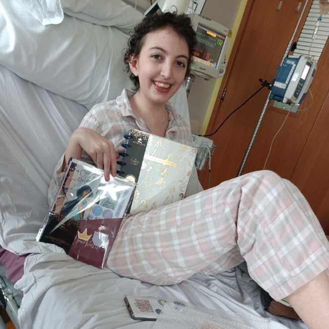 Ellie, dressed in pink pyjamas and smiling from her hospital bed.