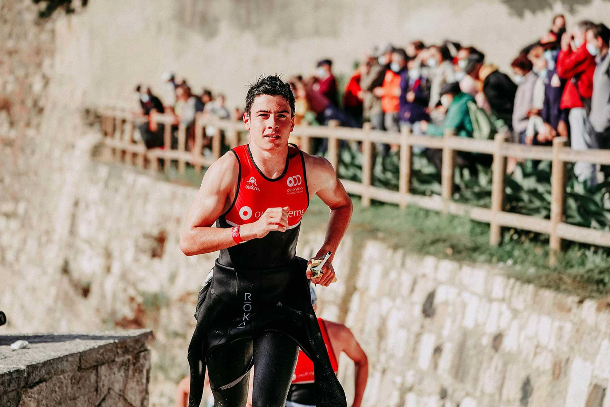 A triathlon runner, still wet from having emerged from his swim, with spectators in the background.