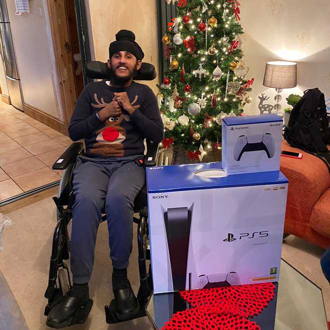 A smiling Sunil posing in front of the Christmas tree with his PS5.