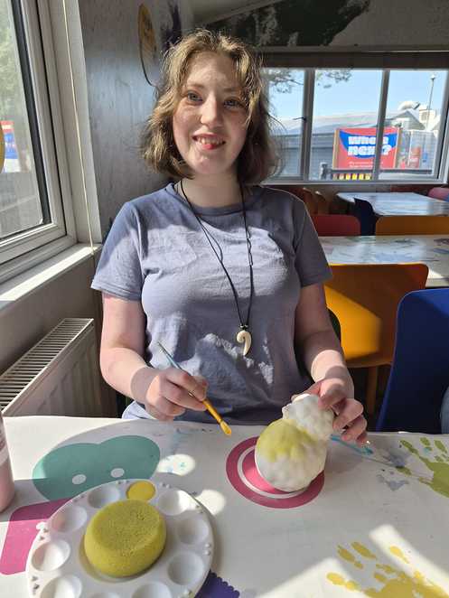 Millie smiles as she decorates a ceramic shape with yellow paint