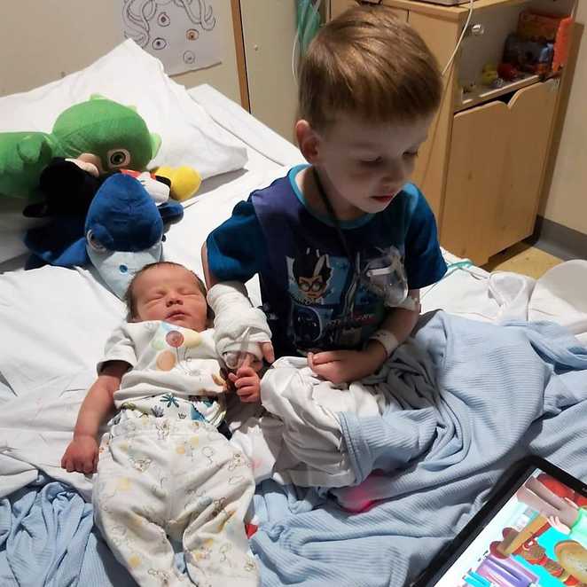 Aiden holding the hand of his younger brother, Logan in hospital shortly after his birth.